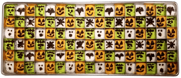 A tray of halloween themed brownies with faces drawn on them.