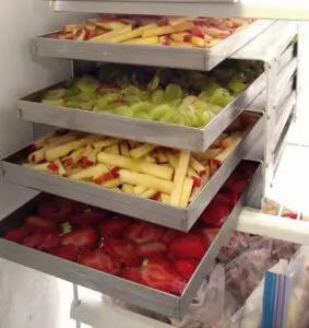 A refrigerator filled with trays of fruits and vegetables.